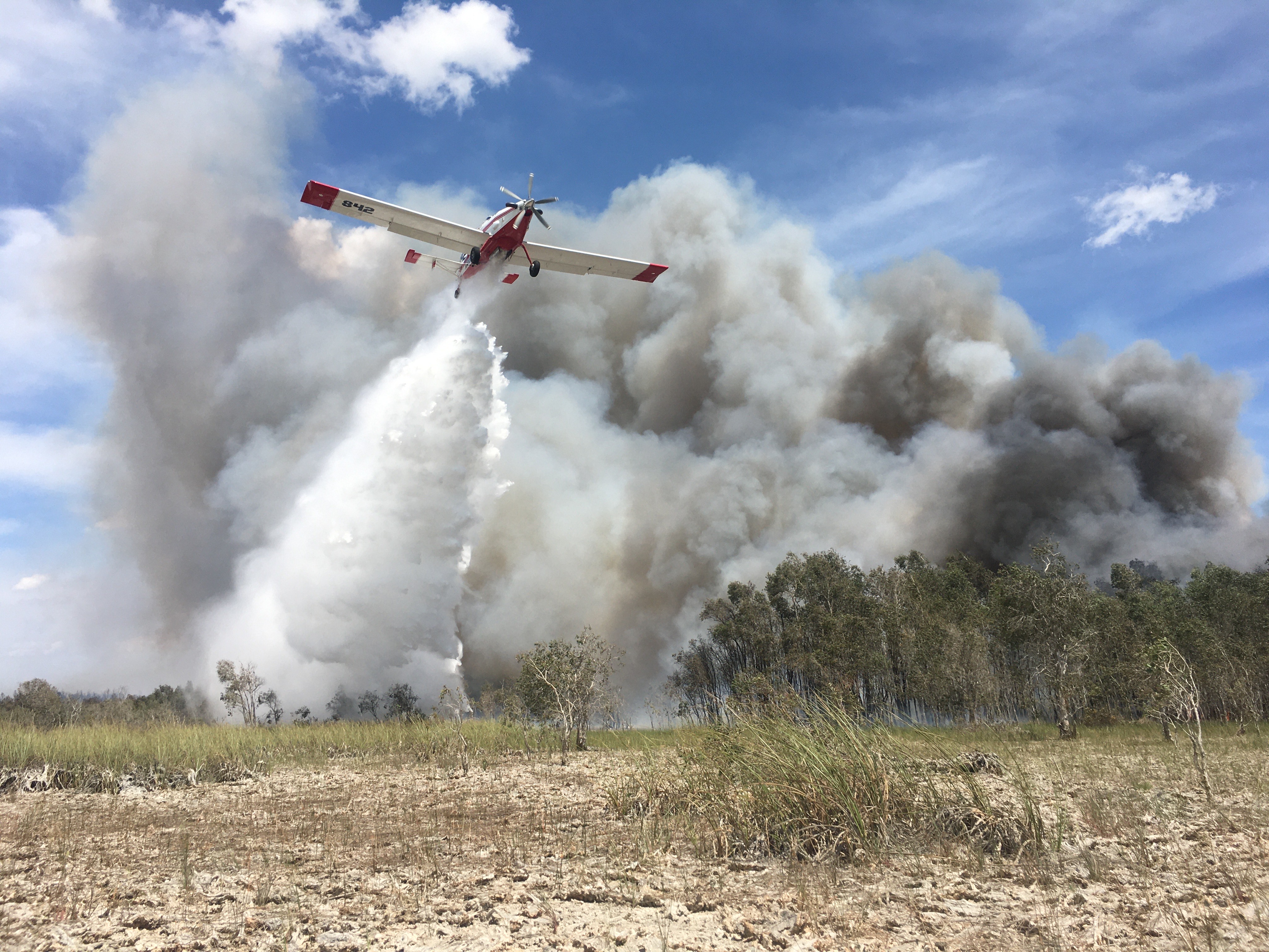 SEAT drops water on Sunday Afternoon Fire in Everglades National Park - NPS photo Josh Pargas Airplane in flight drops water on the grass as white and gray smoke billows up behind. Blue skies above.