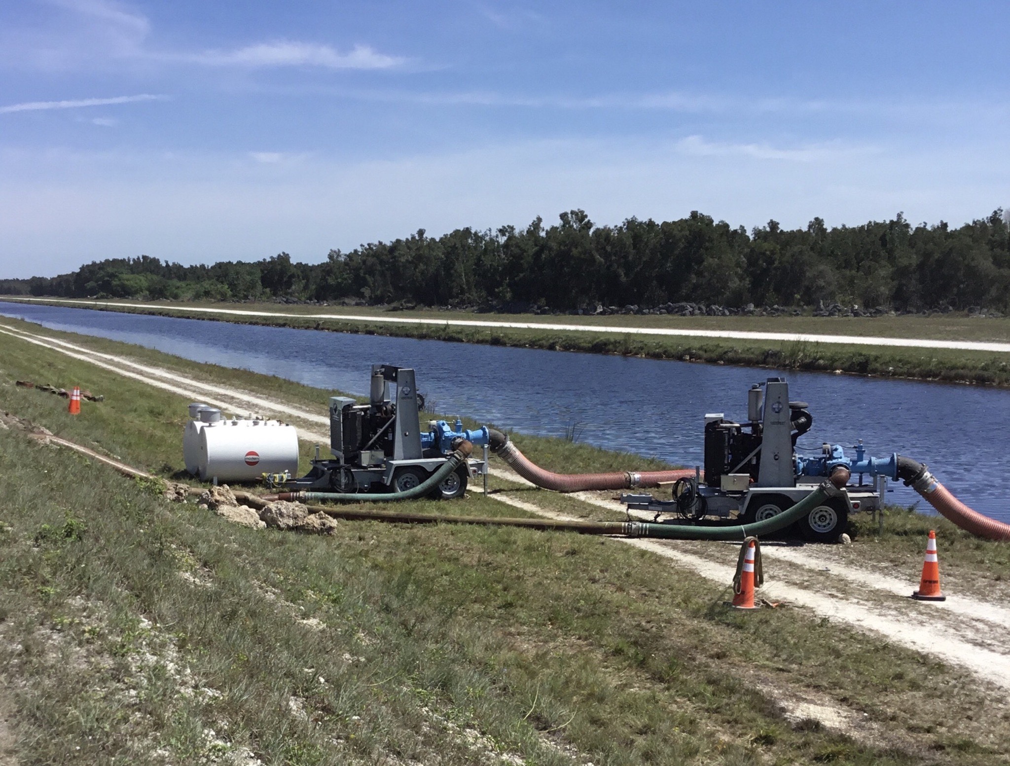 SFWMD Temporary Pump - NPS Photo Reggie Bray Temporary pumps and hoses sit on grass between the canal behind and the levee on the left