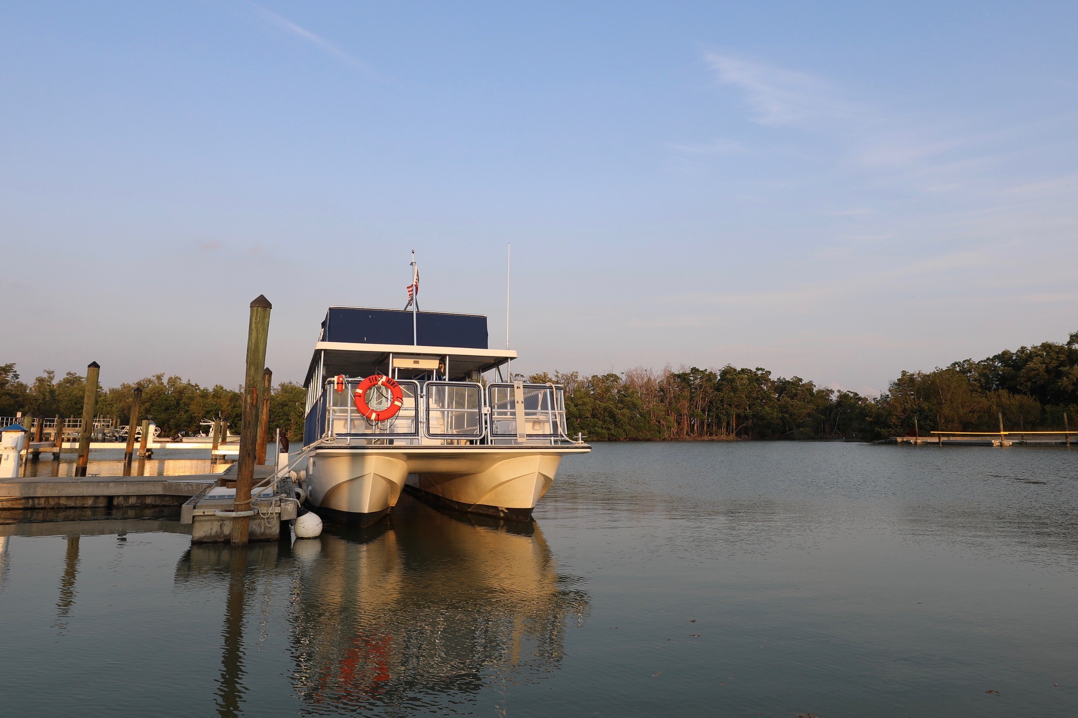 A tour boat docked at the Flamingo Marina in Everglades National Park. The sky is blue and mostly clear and there are mangrove trees in the background.