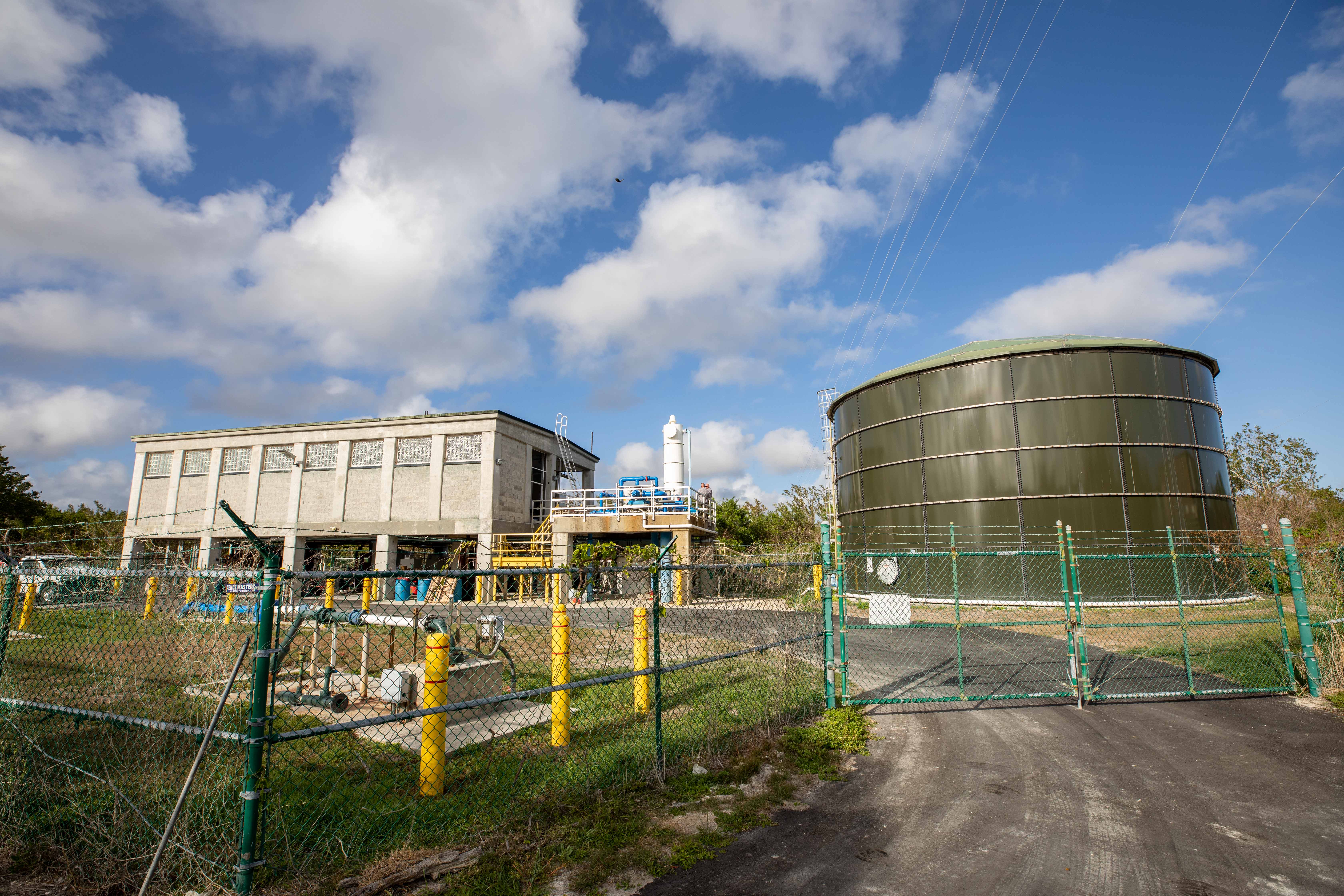 A chain link fence surrounds an elevated building that houses the water treatment facility and a large water tank.