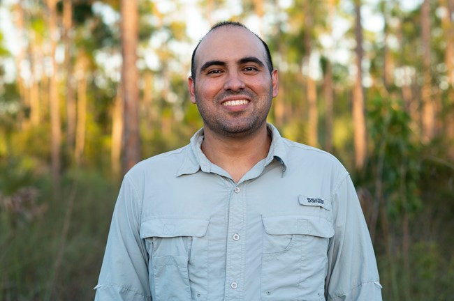 Close-up photo of Anthony Sleiman smiling with blurry trees behind him.