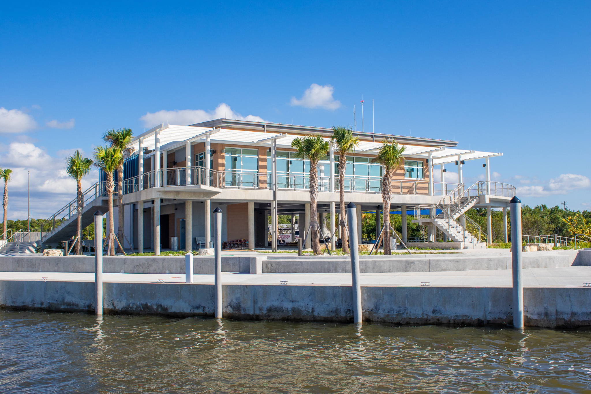 Artist rendering of the Marjory Stoneman Douglas Visitor Center and plaza. Two story modern building has various textures and architectural elements of interest. View of bay behind.