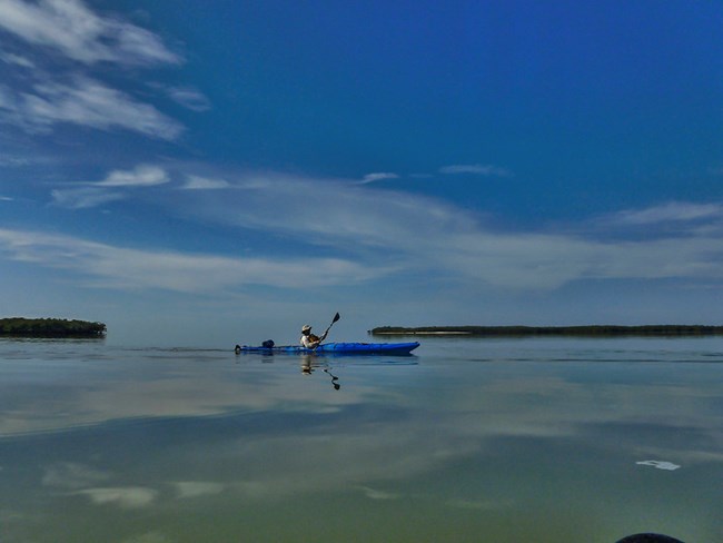 A person in a blue kayak paddles over calm water.
