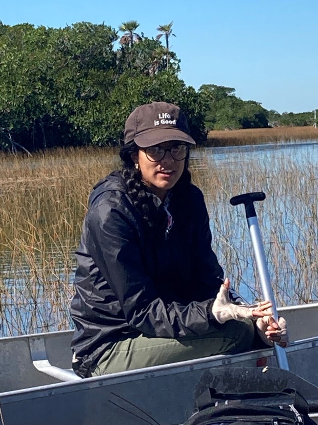 Visitor listening to an Everglades National Park Institute Naturalist speaking in a canoe during the Paddling in the Park program at Nine Mile Pond.