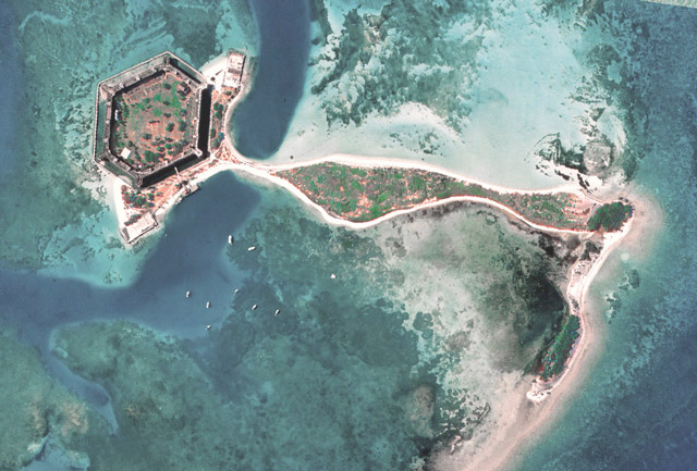 As you slide through the images, you first see a 2003 view of a hexagonal fort with a little bit of white sandy barrier island around it. That island is connected to another L-shaped island. Green vegetation is on the inside of the fort and center of the islands. Next, you see the same view as before, but in 2007 the island with the fort on it is separated from the L-shaped island. The L-shaped island is thinner in places and has less vegetation. Finally, you again see the same view, but in 2013, the islands are connected again. Vegetation is slightly larger than in 2007.