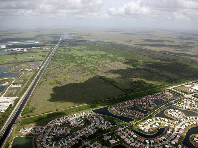 An aerial photo of green open space adjacent roads and developments of cul-de-sacs full of houses. Water containment ponds are nearby.
