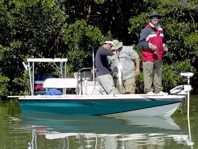 Three fishermen aboard a powerboat, one with a large fish.