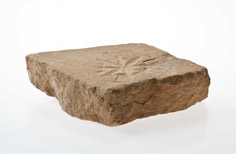 Side view of piece of stone with dial pattern indented on it.