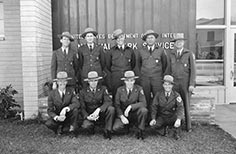 Nine Rangers in uniform pose for a photo in front of a National Park Service building.