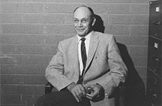 Man sits on a chair smiling with lighter and cigarette in his hands.