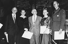 Three men and two women smile and pose for photo while they each hold a sheet of paper.