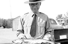 Man in uniform holds up a fish with both hands.