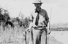 Man holds up a fish in one hand and a fishing pole in another.