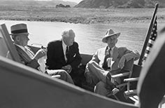 Three men sit in boat on a lake with an American flag attached.