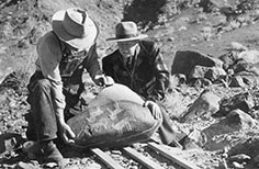 Two men kneeling down with their hands on a large rock with petroglyphs.