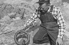 Man kneeling down with aged ringbolt attached to a canyon wall in his hand.