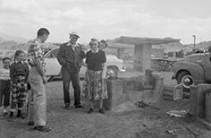 Group of people stand next to barbeque at a picnic area.