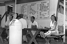 Woman sits at a picnic table with her feet up on the bench in front of a restaurant.