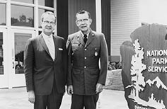 Two men stand beside a National Park Service sign.