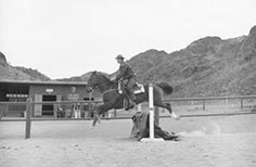 Man in uniform rides a horse while they jump over a picket fence.