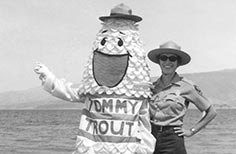 Woman in uniform poses next to person in a fish shaped mascot costume.