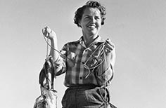 Woman stands holding a string of fish on a rope.