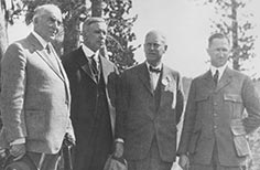 Four men in suits and uniform pose for a photo.