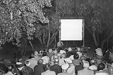 Uniformed Ranger gives a projection screen presentation outdoors to a small group of people.