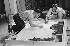 Two men with their heads down as they use their hands to sculpt the mould for the relief model.