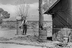 Older gentleman using his hand to display the height of water damage caused by the flood on a  rectangular pump, with a barn-like shed to the right.