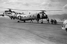 Five men wearing hard hats and carrying equipment board a U.S. Air Force Rescue helicopter. 