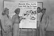 Four uniformed Coast Guard Auxiliary Officers pose on both sides of an enlarged newspaper clipping that reads Maverick Wins, Seattle Loses Gold Cup To Vegas.