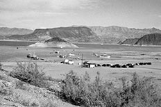 Serpentine shaped shoreline at left, lake with many moored boats to right, mountains and clouds in distance.