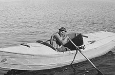 A man in a hat rows a boat on a lake.