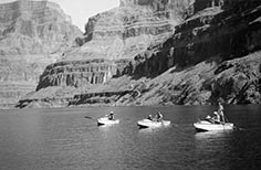 Three boats on river with people on them and mountains in the background.