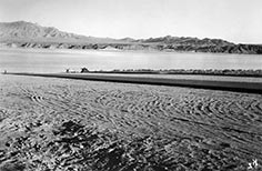 Single car and tent in distance on lake beach with mountains in the background.