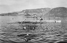 People swim around and sit on a small floating dock on a lake.