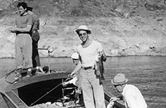 Five men fishing in a boat while one of them smiles and holds up a fish.