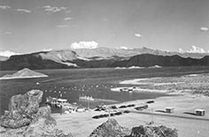 Two docks on lake by mountains with parking lot of cars in foreground.