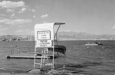 Lifeguard stand on beach by lake with people on floating dock.