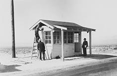 Small building with three people standing by it, one on a ladder.