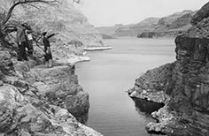 People stand on cliff overlooking a lake and mountains.