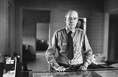 Man in uniform poses in front of a map under glass surface.