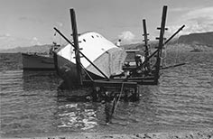 Boat tipped over into lake with men working next to it.