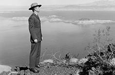 Man in uniform stands on cliff looking over a lake.