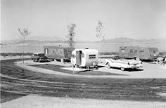 Cars and travel trailers next to a lake.