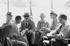 Six men sit with flagpoles behind them.