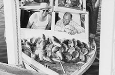 Six men pose for photo on a boat with dozens of fish lined up on it.