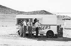 Four people stand by a hamburger stand.