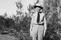 Man in uniform standing in front of foliage.